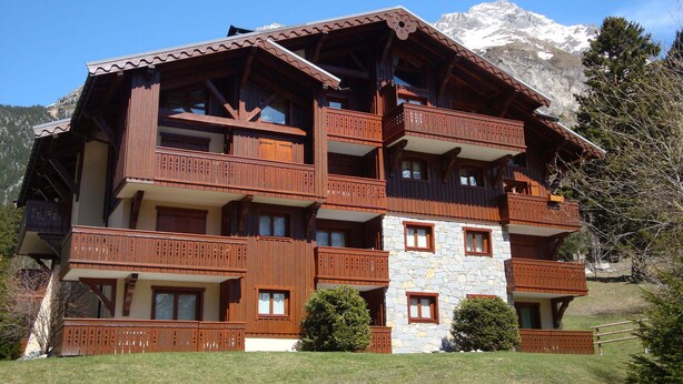 Un chalet en bois à plusieurs étages, doté de balcons, d’une façade en pierre et surplombant un paysage montagneux.