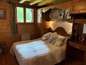 Une chambre à coucher dans une cabane en bois, avec un lit, une table de chevet, une commode et une fenêtre avec des rideaux.