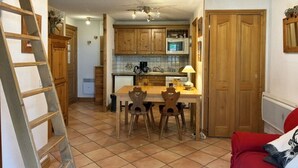 Une cuisine avec des meubles de rangement en bois, une table à manger avec des chaises, un canapé rouge et une échelle appuyée contre le mur.