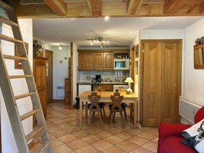 Una cocina con armarios de madera, una mesa de comedor con sillas, un sofá rojo y una escalera apoyada en la pared.