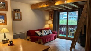 Une pièce chaleureuse avec une table en bois, un canapé rouge et une fenêtre donnant sur un balcon.