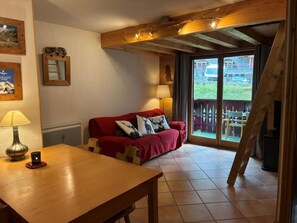 Una habitación acogedora con una mesa de madera, un sofá rojo y una ventana con vistas a un balcón.