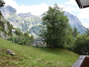 Paisaje montañoso con un edificio en primer plano, un cartel que indica 'Accès Interdit' y un árbol grande.