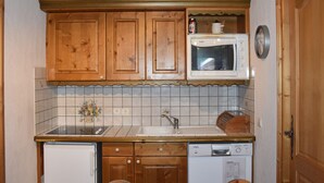 Une cuisine compacte dotée de meubles en bois, d’un four à micro-ondes, d’un évier et d’un lave-vaisselle.