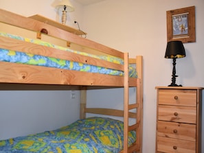 Un lit superposé avec une structure en bois, une lampe sur le lit supérieur et une commode avec des tiroirs.