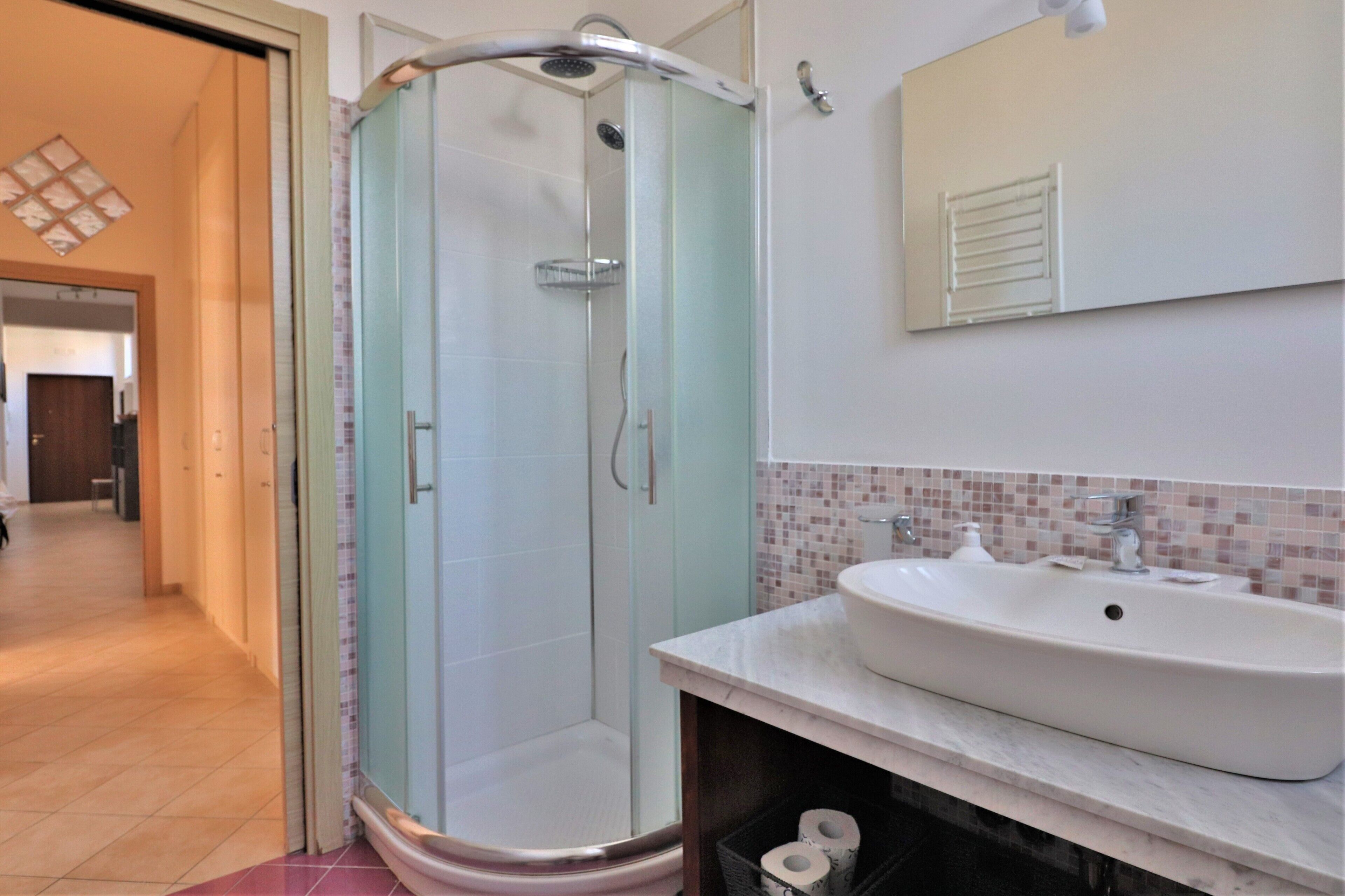 Une salle de bain moderne avec une douche à parois de verre, un lavabo blanc et un mur recouvert de carreaux.