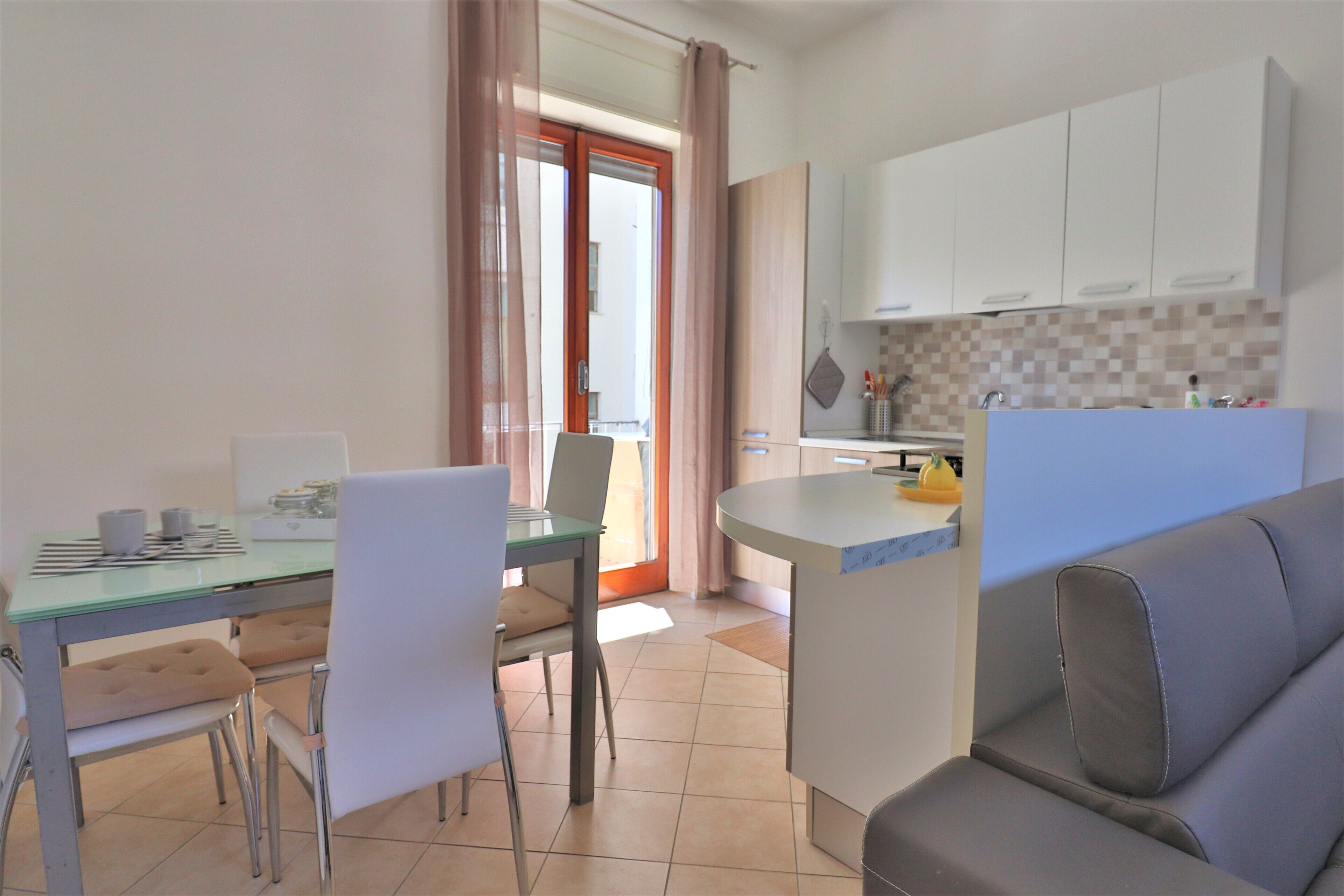 Une cuisine moderne avec des meubles blancs, une table à manger avec des chaises et un petit îlot central doté d’un évier.