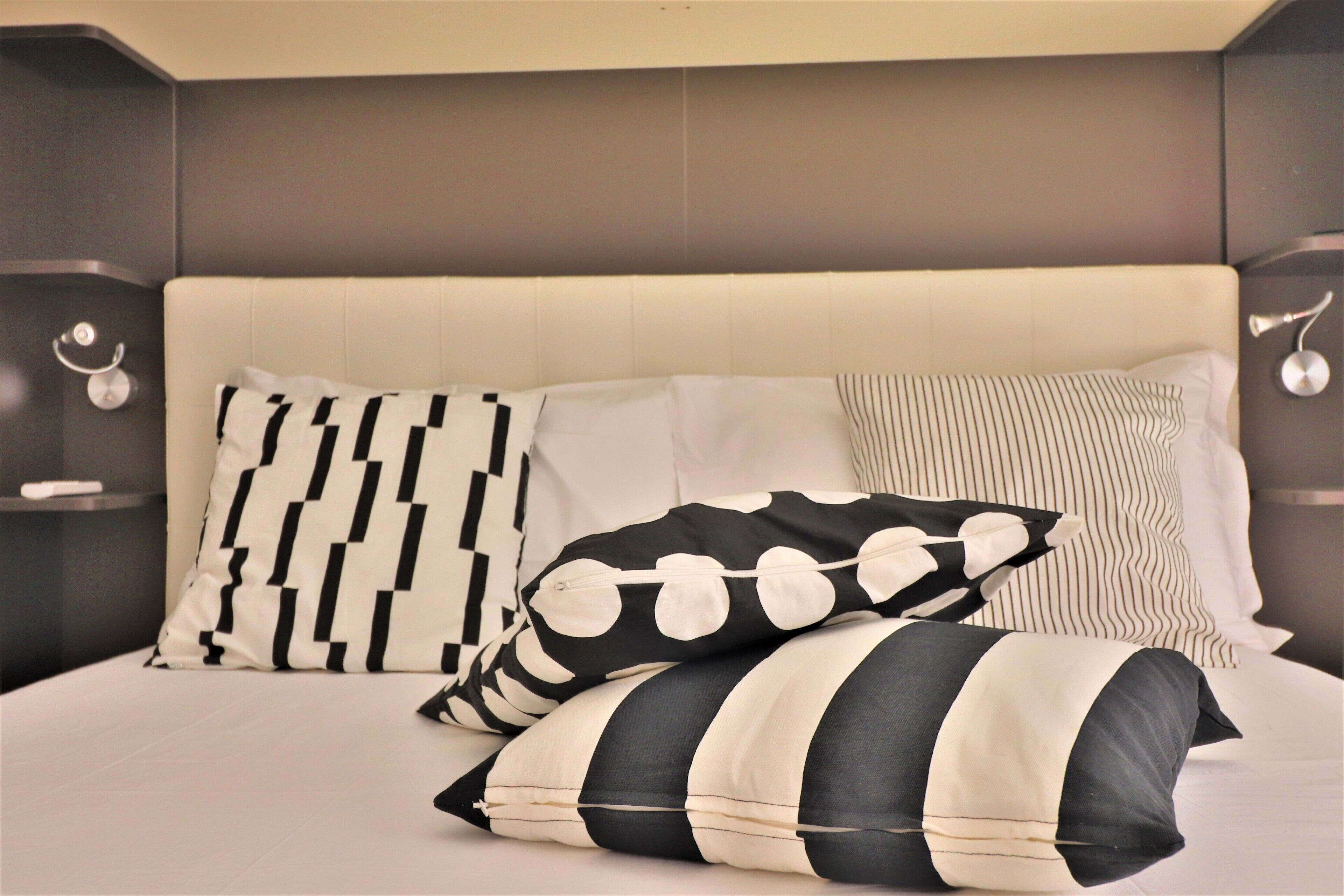 Uma cama com cabeceira estofada, vários travesseiros com diferentes estampas e mesas de cabeceira com abajures.