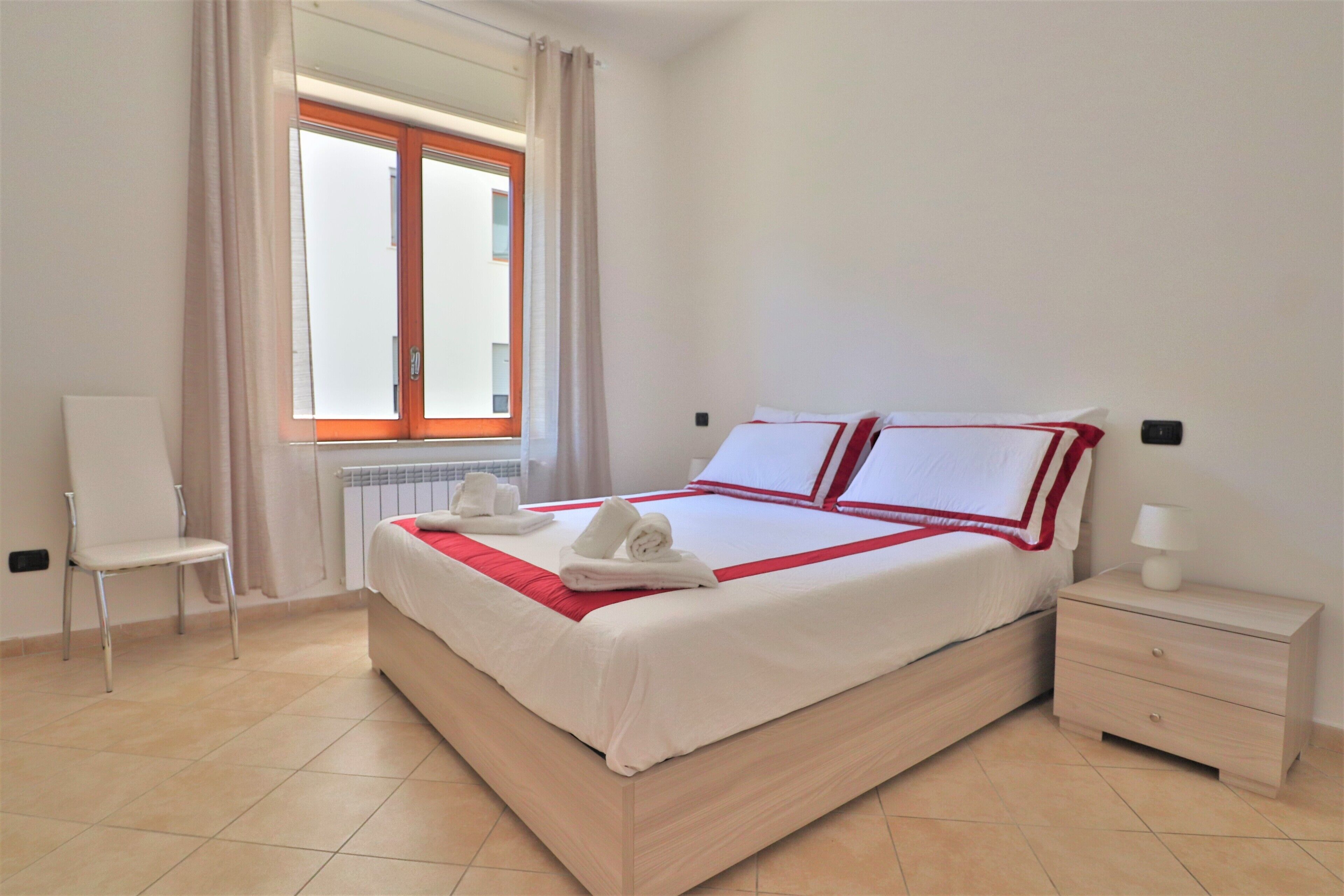 A neatly arranged hotel room with a bed, a chair, a nightstand, and a window with curtains.