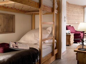 A bunk bed with a wooden frame, a small bedside table with a lamp, a red chair, and a wall-mounted shelf with a picture frame. - Courchevel 1850 Ski-in/ski-out studio with parking and wifi (Courchevel 1850)