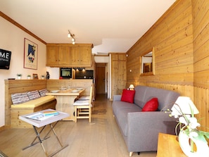 A cozy room with wooden walls, a grey sofa, a wooden dining table with chairs, and a small kitchen area. - Courchevel 1850 Ski-in/ski-out studio with parking and wifi (Courchevel 1850)