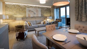 Ein modernes Wohnzimmer mit einer Steinwand, einem Sofa, einem Esstisch für zwei Personen und einem großen Fenster mit Vorhängen.