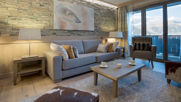 Ein modernes Wohnzimmer mit Steinwand, einem großen Gemälde, einer Couch, einem Couchtisch und Bergblick durch große Fenster.