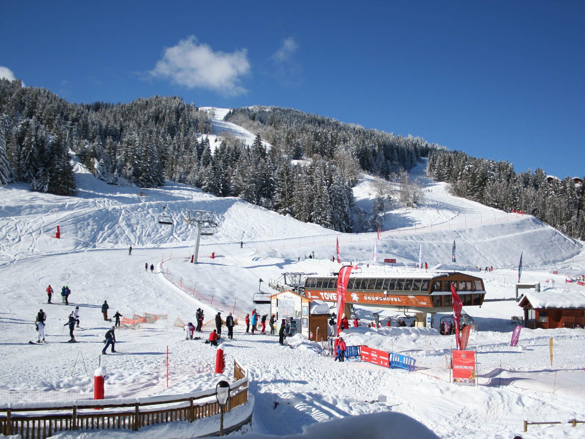 A ski resort with a chairlift, snow-covered slopes, and a building with signage.
