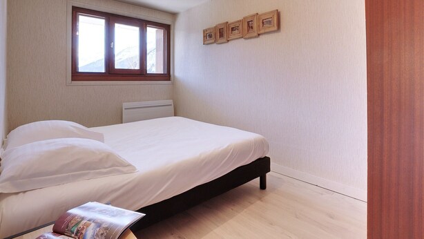 Un dormitorio con cama, ventana y un cuadro colgado en la pared.
