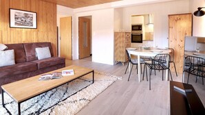 Una sala moderna con techo de madera, un sofá de cuero marrón, una mesa de centro de madera y un comedor con mesa blanca y sillas negras.