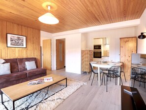 A modern living room with a wooden ceiling, a brown leather sofa, a wooden coffee table, and a dining area with a white table and black chairs. - Charming apartment in central Courchevel 1550, direct access to Courchevel 1850 (Courchevel 1550)