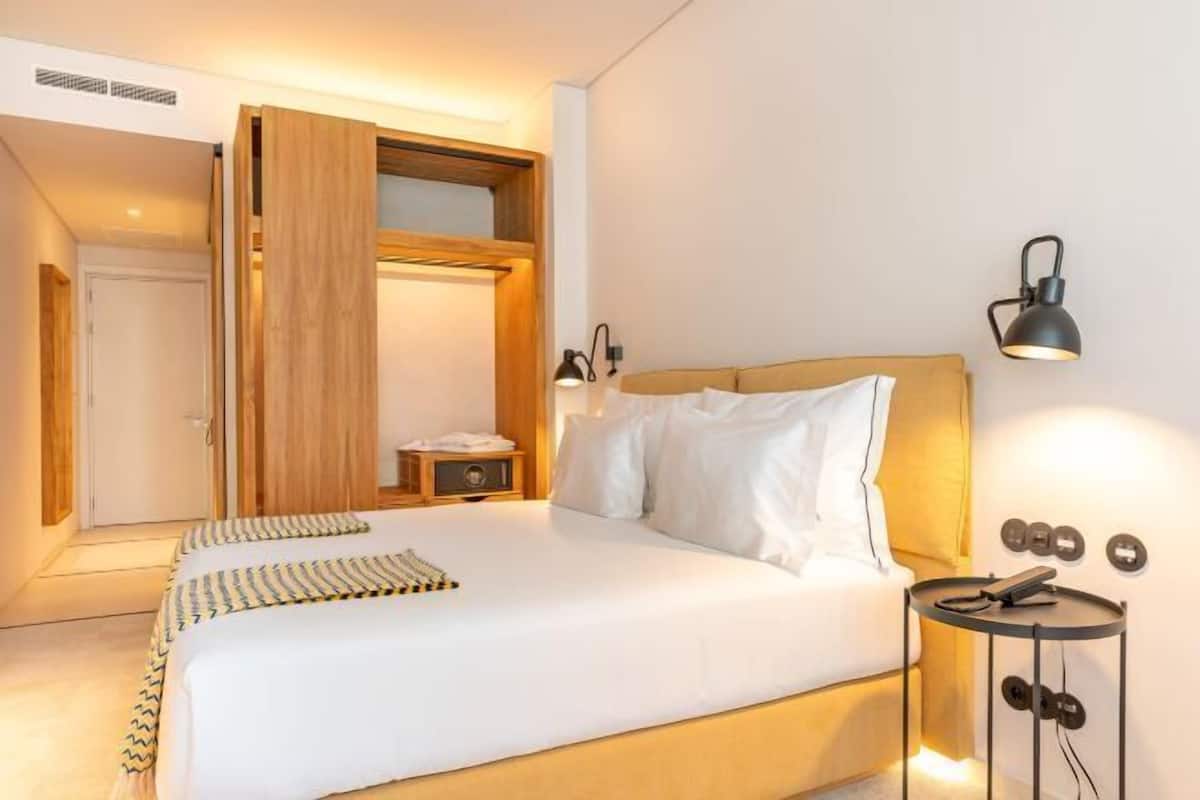 A bedroom with a bed, bedside lamps, a small table, and a wardrobe.