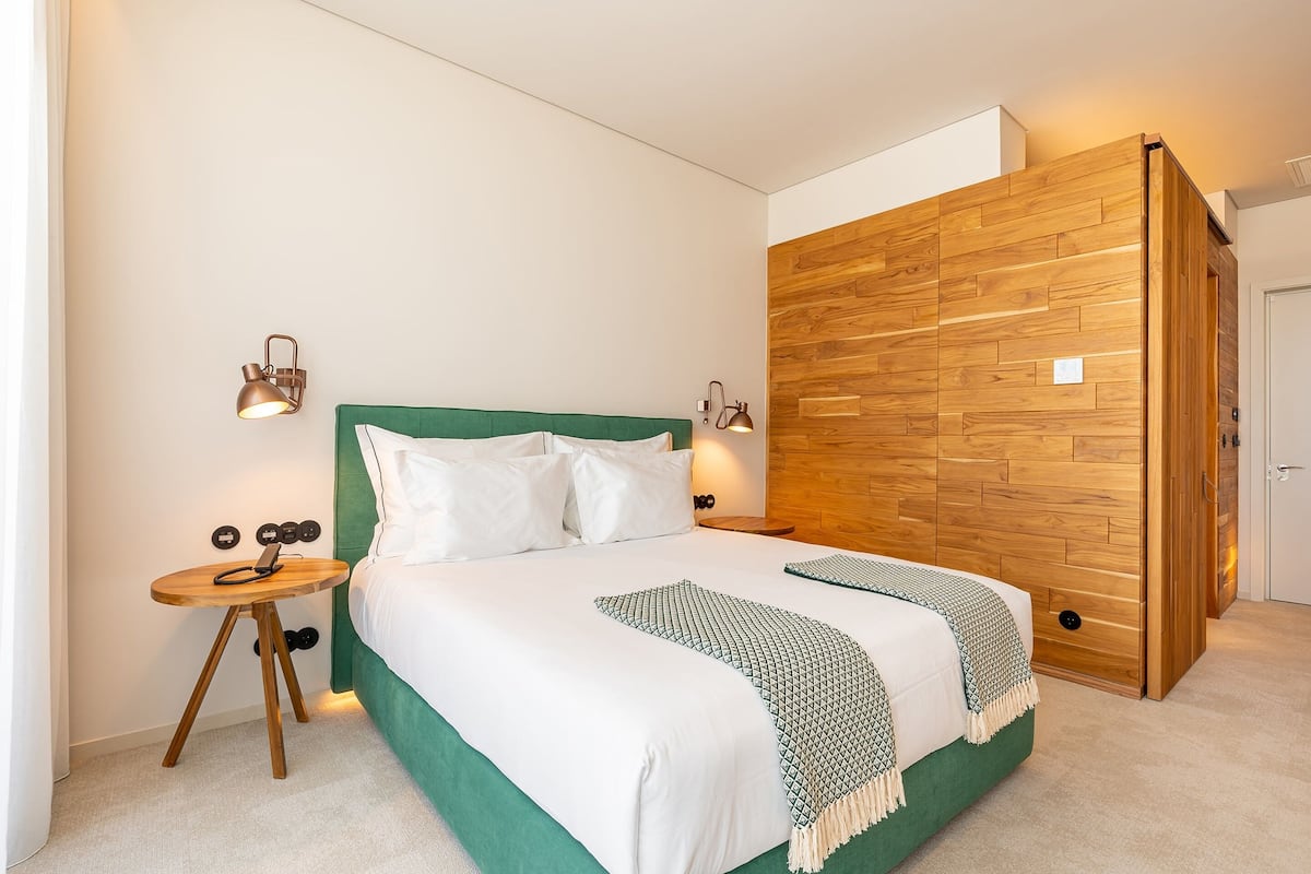 A modern bedroom with a green upholstered headboard, a wooden accent wall, and a small bedside table with a lamp.