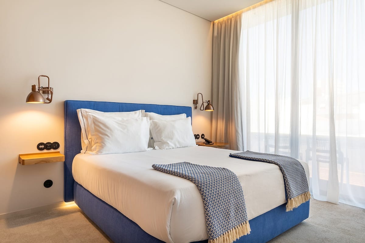 A modern hotel room with a blue headboard, white bedding, and two bedside lamps.