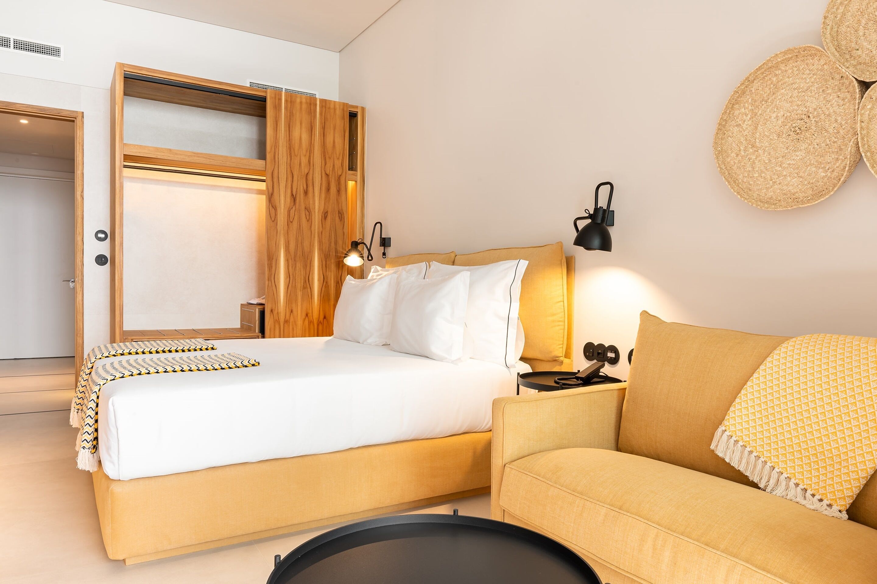A modern bedroom with a bed, a sofa, a bedside table, and a wall-mounted lamp.