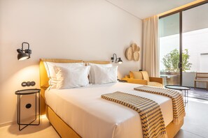 A hotel room with a large bed, two bedside lamps, a small side table, a sofa, and a balcony with a view.