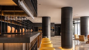 A modern bar area with a long counter, multiple stools, and a unique lighting fixture above.