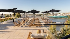 A rooftop lounge area with sun loungers, umbrellas, and potted plants.