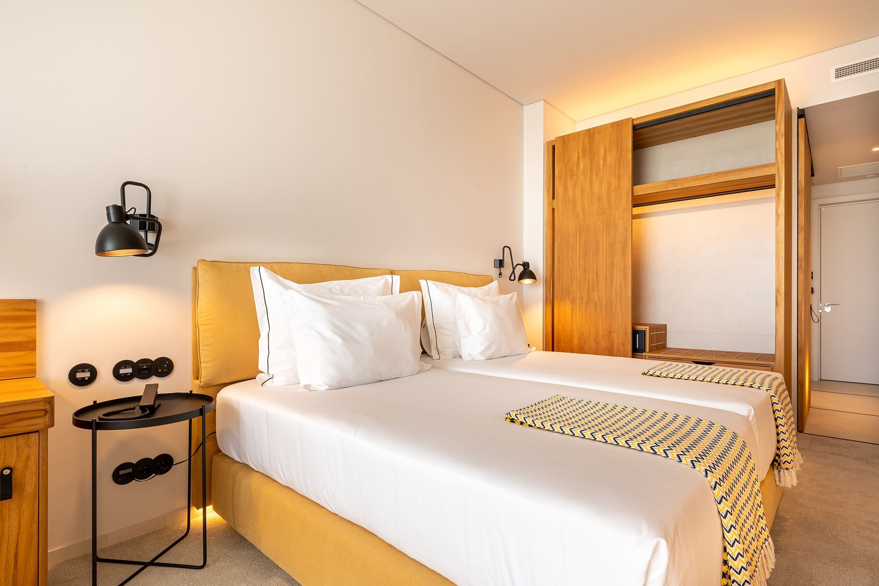 Una habitación de hotel con una cama doble, dos mesitas de noche, un armario y un espejo.