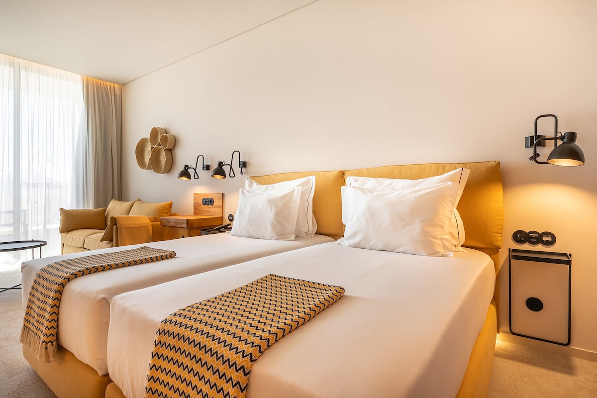 A hotel room with two beds, a sofa, a desk, and a lamp.