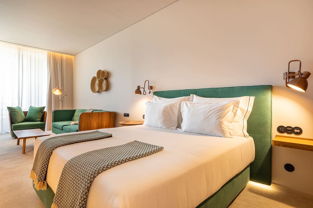 A hotel room with a large bed, a green upholstered sofa, a small table, and a lamp.