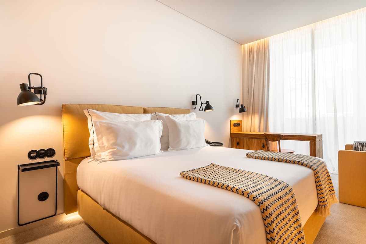 A hotel room with a large bed, bedside lamps, a wooden nightstand, and a desk.