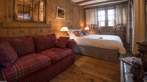 A wooden room with a plaid sofa, a bed with white bedding, and a window with curtains. - Elegant duplex in Courchevel 1850 with fireplace and private parking (Courchevel 1850)