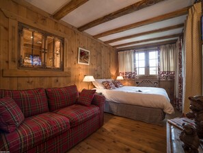 Une pièce en bois avec un canapé à carreaux, un lit avec une literie blanche et une fenêtre avec des rideaux.