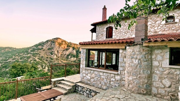 A stone building with a red-tiled roof, a wooden deck, and a view of a mountainous landscape. - Archontiko Kolokotroni (Gortynia)