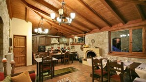 A rustic interior with exposed wooden beams, a stone fireplace, and a dining area with wooden furniture. - Archontiko Kolokotroni (Gortynia)