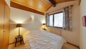 Ein Schlafzimmer mit Holzboden, einem großen Bett, zwei Nachttischlampen, einem Fenster mit Vorhängen und einer Heizung.