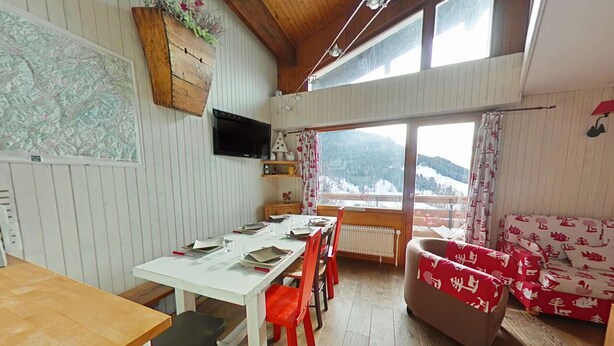 Ein Essbereich mit Holztisch und Stühlen, einer Couch, einem Heizkörper und einem Fenster mit Blick auf eine verschneite Landschaft.