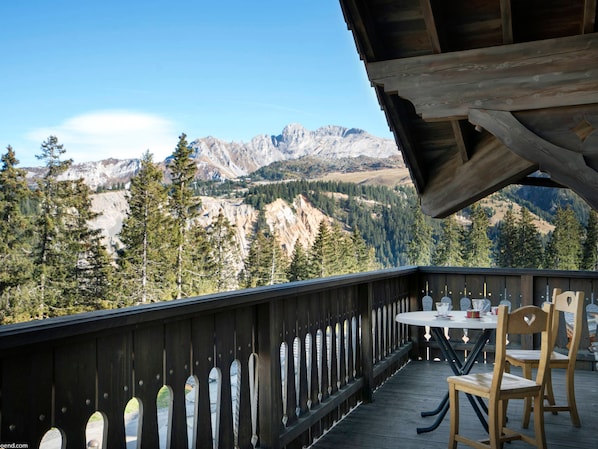 A wooden deck with a table and chairs, overlooking a mountainous landscape.