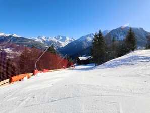 Une piste de ski enneigée, bordée d’une clôture en bois et protégée par un filet rouge.