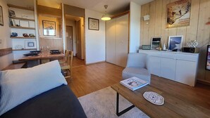 Ett modernt vardagsrum med en soffa, ett soffbord och en matplats med ett bord och stolar. Där finns ett vitt skåp med en radio och dekorativa föremål ovanpå.
