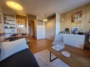 A modern living room with a sofa, a coffee table, and a dining area with a table and chairs. There is a white cabinet with a radio and decorative items on top. - Renovated family apartment in Courchevel 1550, 3 rooms (Courchevel 1550)