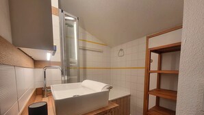 Ett modernt badrum med en vit tvättställsskål, ett badrumsskåp i trä och en duschkabin med glasväggar.