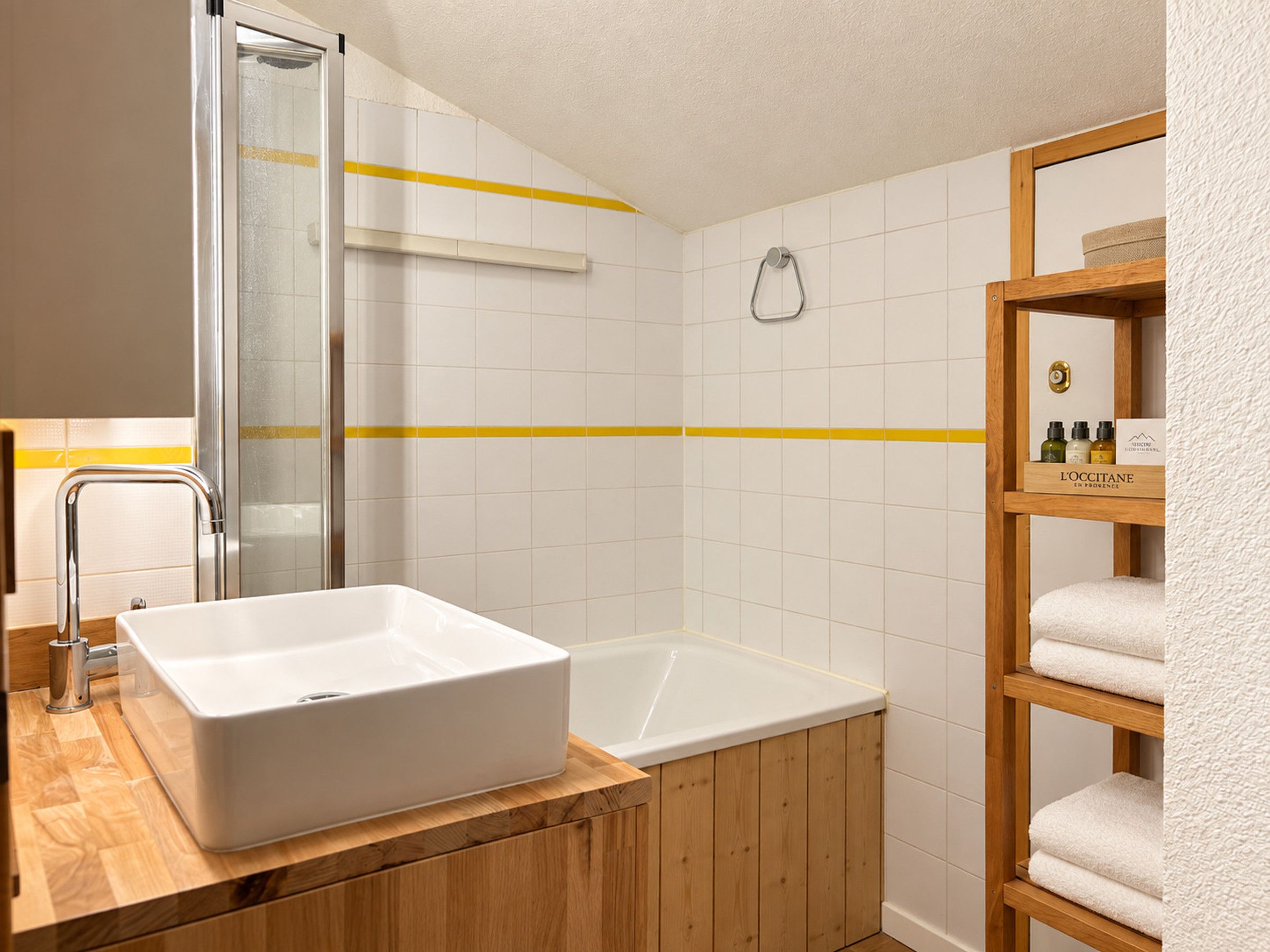 A bathroom with a large white sink, a bathtub, and a wooden shelf with towels.