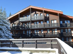 Un bâtiment en bois à plusieurs étages, doté de balcons, qui ressemble probablement à un hôtel ou à un chalet, et qui est entouré d’arbres couverts de neige.