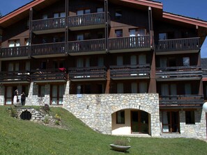 Un hotel de diverses plantes amb balcons, façana de pedra i una pendent coberta d'herba.