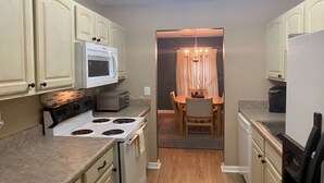 A compact kitchen with a stove, microwave, and a dining area with a chandelier.