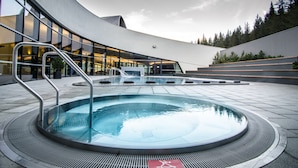 Un bâtiment moderne à l’extérieur incurvé, doté d’un espace piscine central et d’un chemin d’accès aménagé pour les personnes à mobilité réduite.