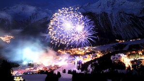 Paisaje nevado de montañas con un pueblo en la falda y un gran espectáculo de fuegos artificiales en el cielo.