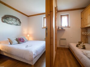 A bedroom with a bed, a bedside table, a lamp, a shelf with decorative items, and a window. - Charming apartment in Courchevel with large terrace (Courchevel 1550)